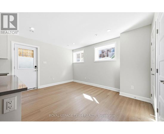 A spacious room with light wood flooring and white walls, with a door on the left and a picture on the wall.