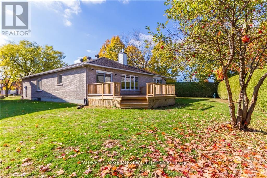 A house with a grey roof and a deck is surrounded by trees with autumn leaves.