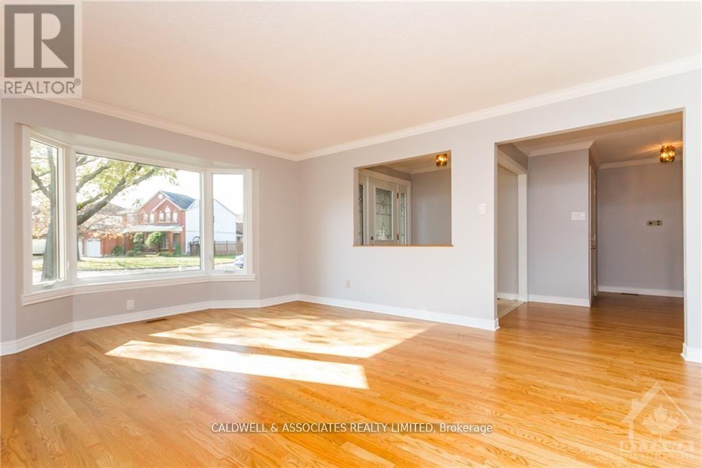 A spacious room with wooden flooring and a large window overlooking a red house.
