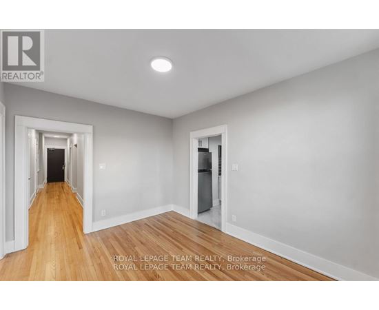 A spacious room with wooden floors and white walls, with a doorway leading to another room.
