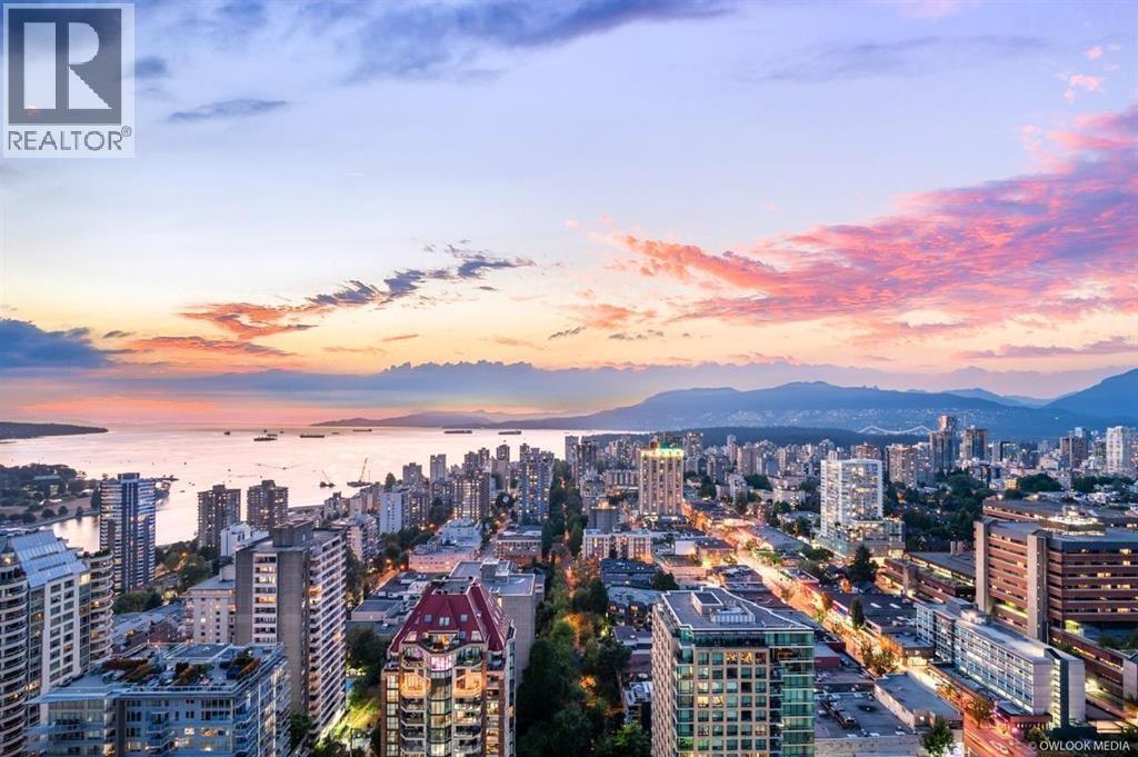 A cityscape at dusk with buildings and a body of water in the foreground.