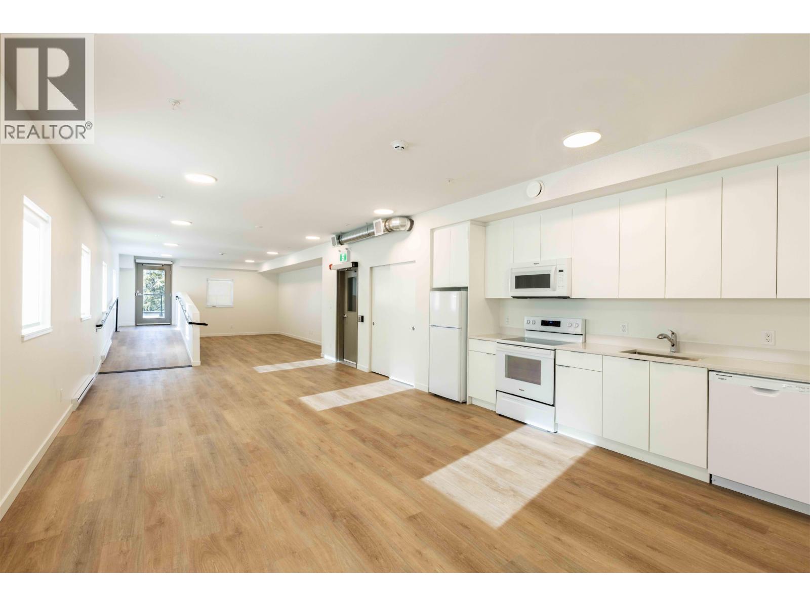 A well-lit kitchen with white cabinets and a wooden floor.