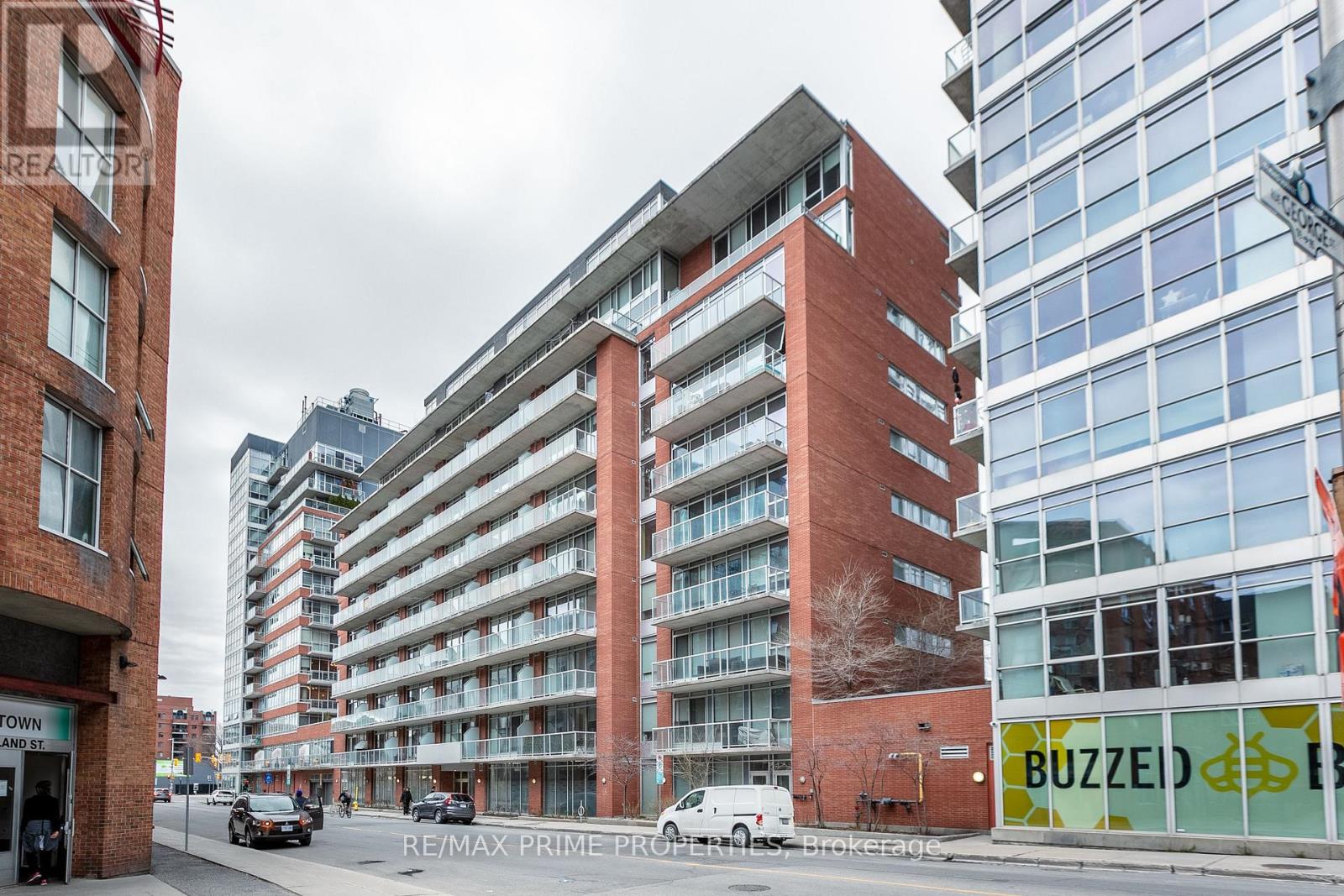 A street view of a city with a red brick building in the foreground and a modern glass building in the background.