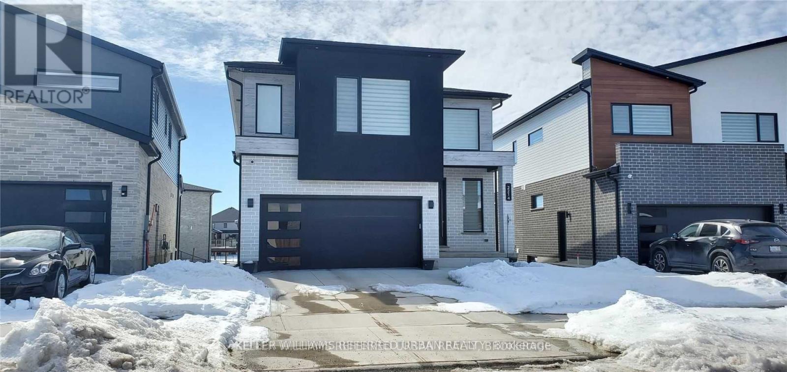 A house with a black garage door is surrounded by snow.