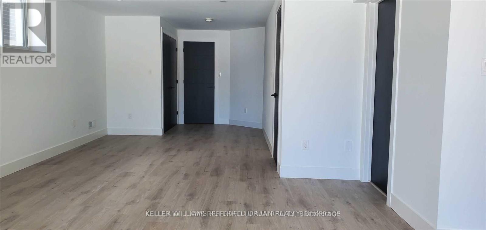 A spacious room with wooden flooring and white walls.