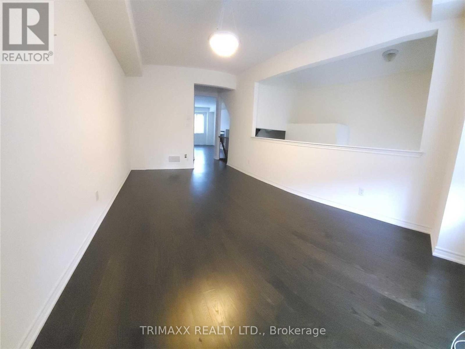 A spacious room with dark wood flooring and white walls, with a mirror on the wall.