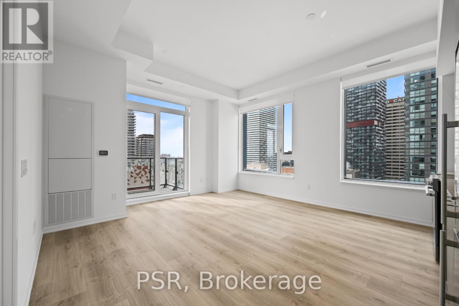 A spacious room with wooden flooring and large windows.
