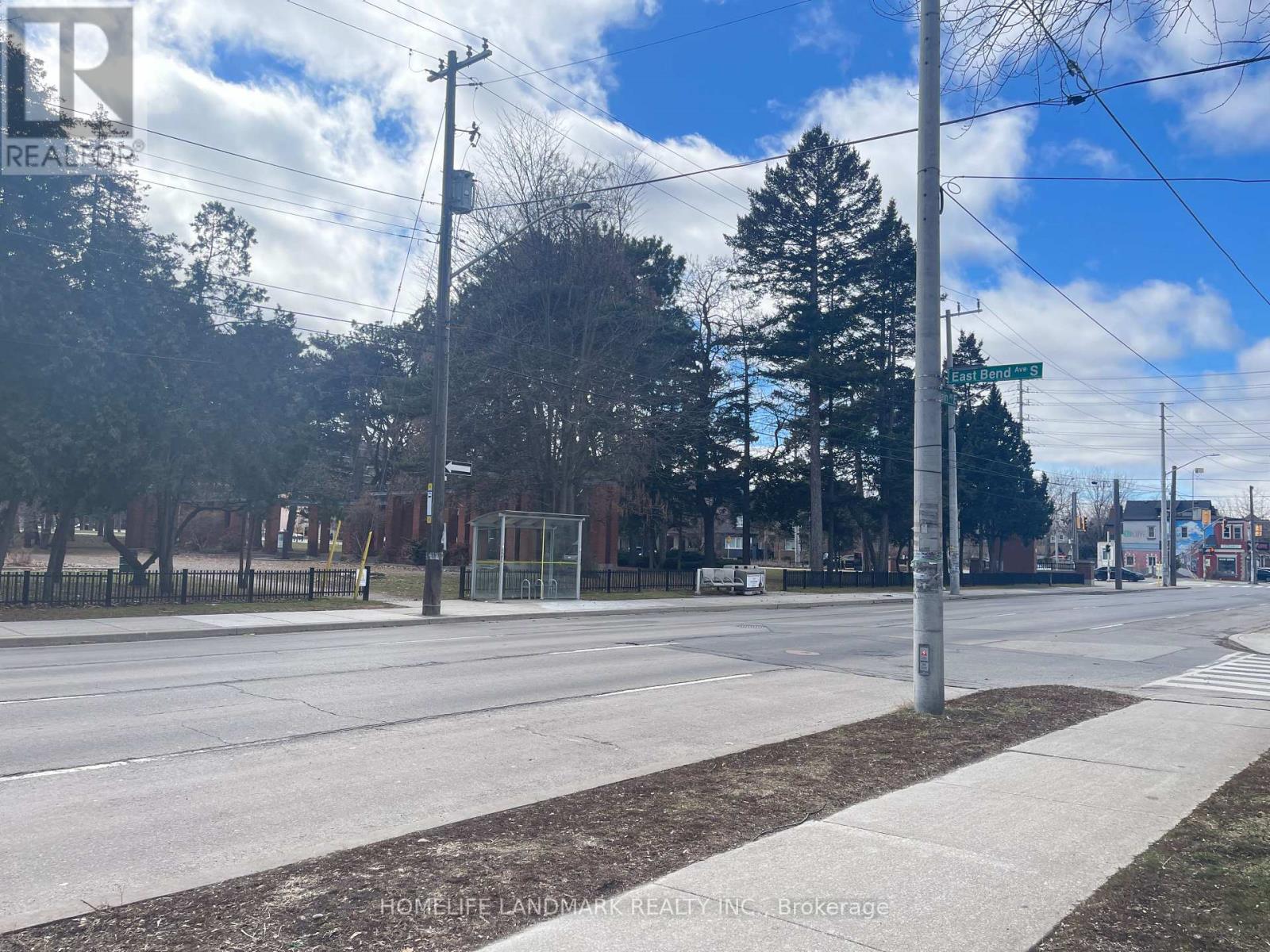 A street view with a sidewalk, trees, and a fence.