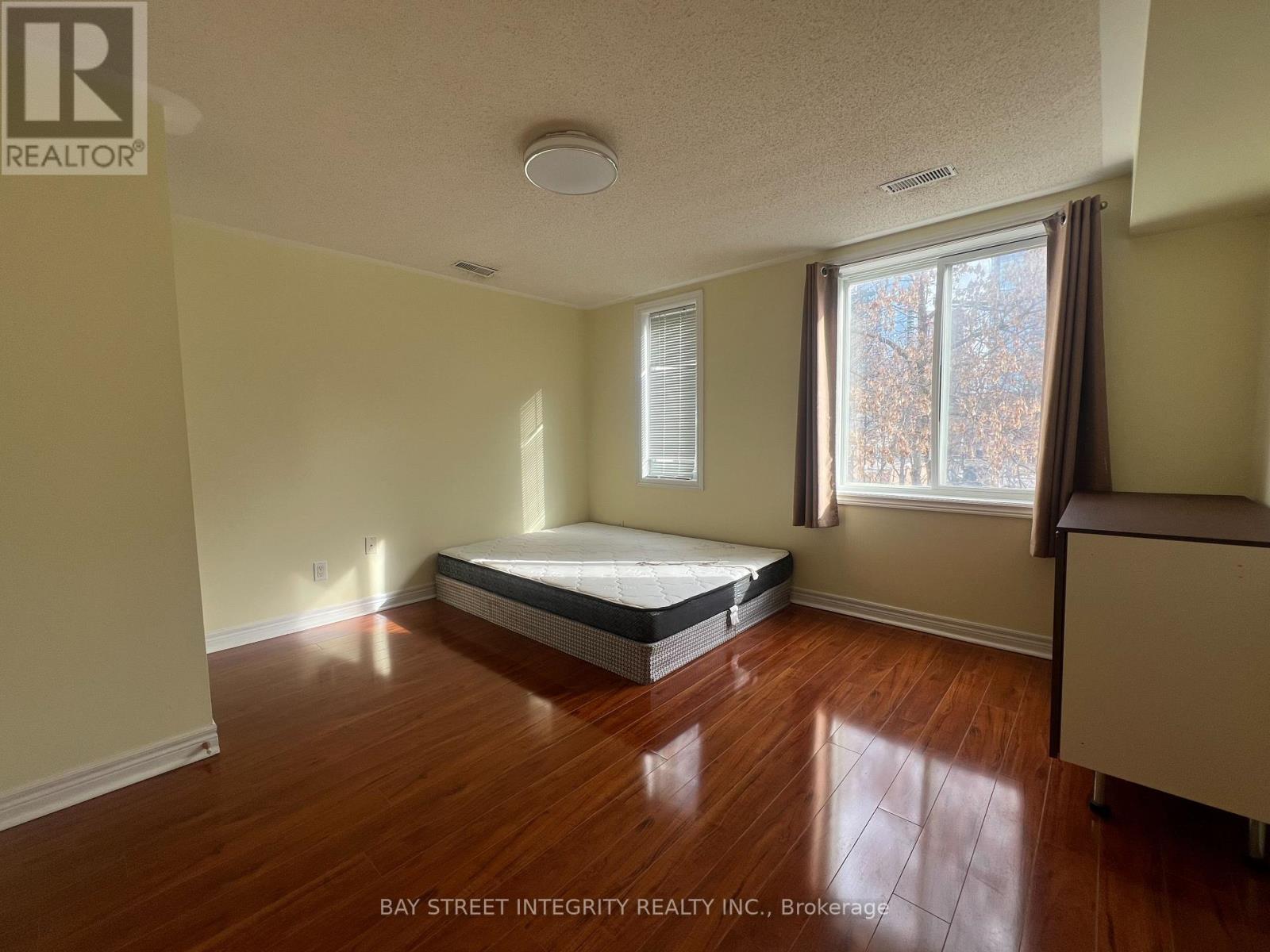 A bedroom with a bed, wooden floors, and a window with a view of trees outside.