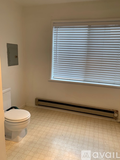 A bathroom with a toilet, window with blinds, and a radiator.