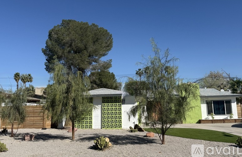 A house with a white fence and a green roof is surrounded by trees and bushes.