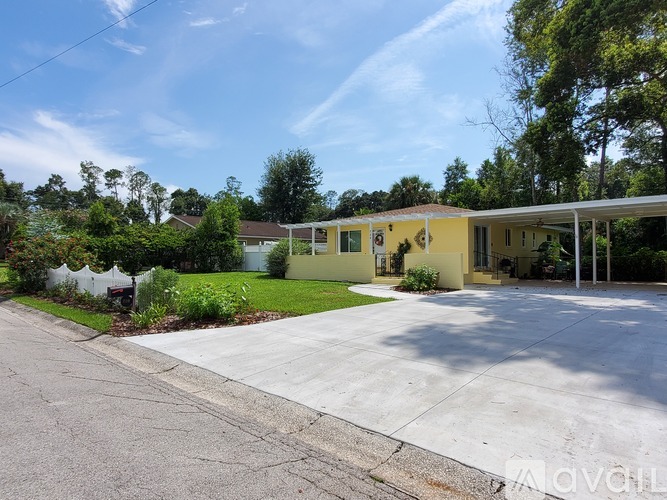 A yellow house with a white fence and green trees in the background.
