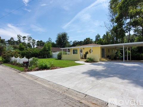 A yellow house with a white fence and green trees in the background.