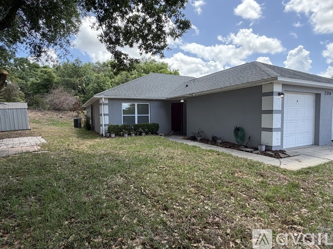 A grey house with a white garage door is surrounded by a grassy area.