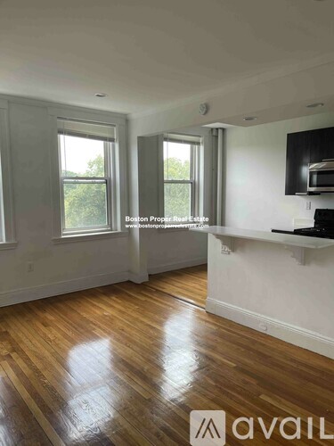 A spacious room with wooden floors and two windows.