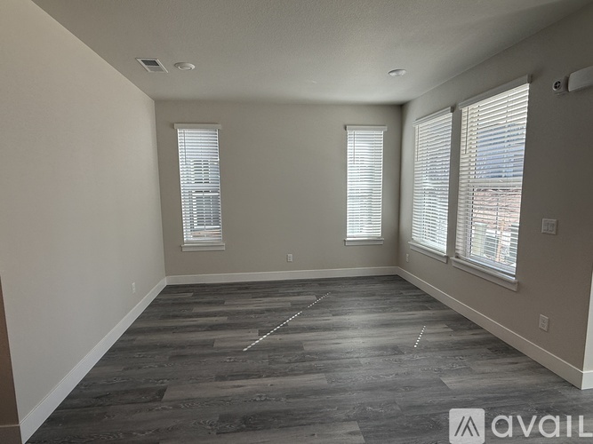 A spacious room with wooden flooring and two windows.