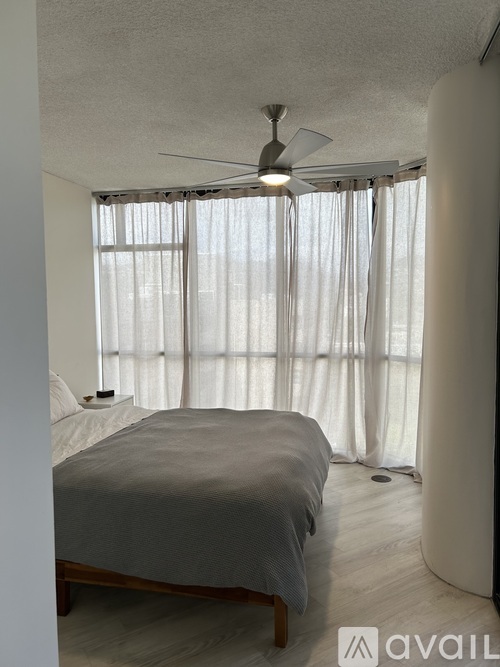 A bedroom with a bed, a ceiling fan, and a window with curtains.