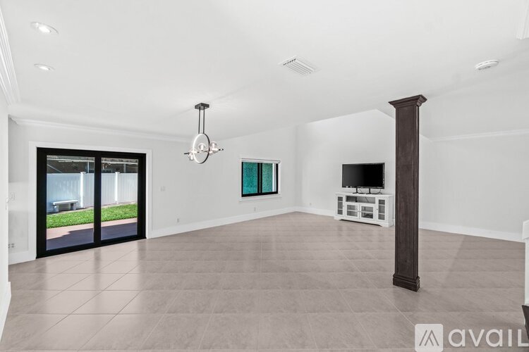 A spacious living room with a television, a chandelier, and a sliding glass door.