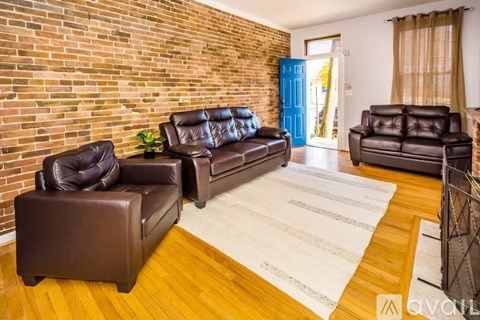 A living room with brown leather furniture and a brick wall.