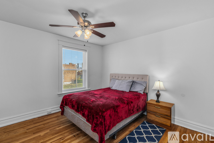 A bedroom with a red bedspread and a ceiling fan.