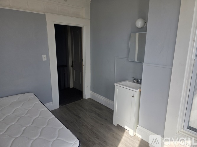A white mattress is on a wooden floor in a room with grey walls.