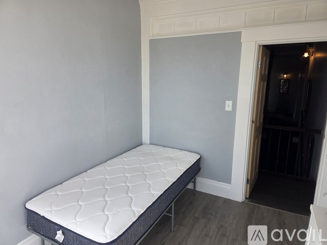 A mattress is placed in a room with grey walls.