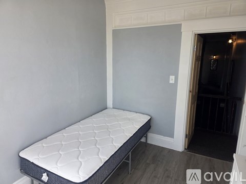 A mattress is placed in a room with grey walls.