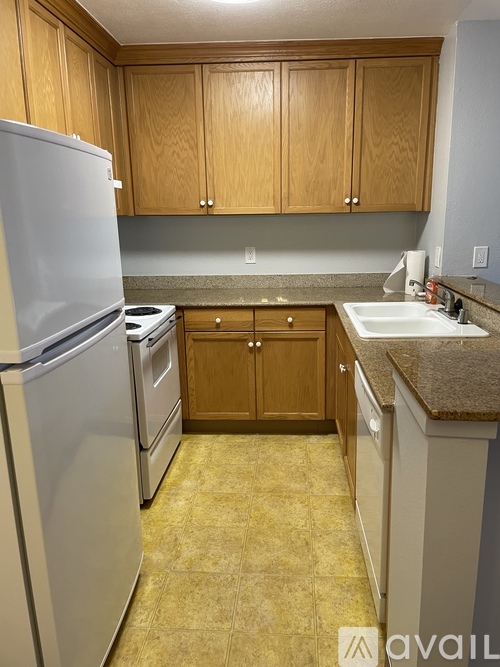 A kitchen with a white refrigerator, brown cabinets, and a granite countertop.
