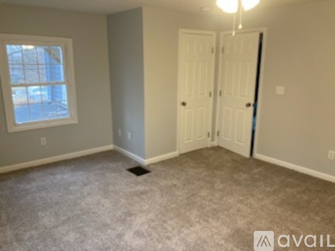 A room with a carpeted floor, two doors, and a window.