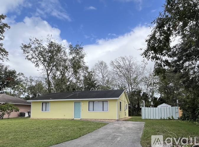 A yellow house with a blue door is surrounded by a white fence and green grass.
