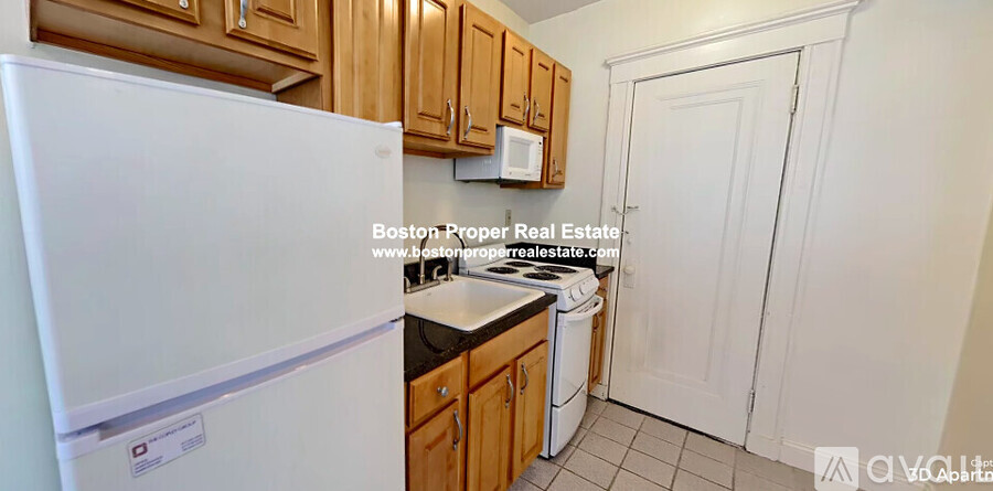 A kitchen with a white fridge, wooden cabinets, and a white door.