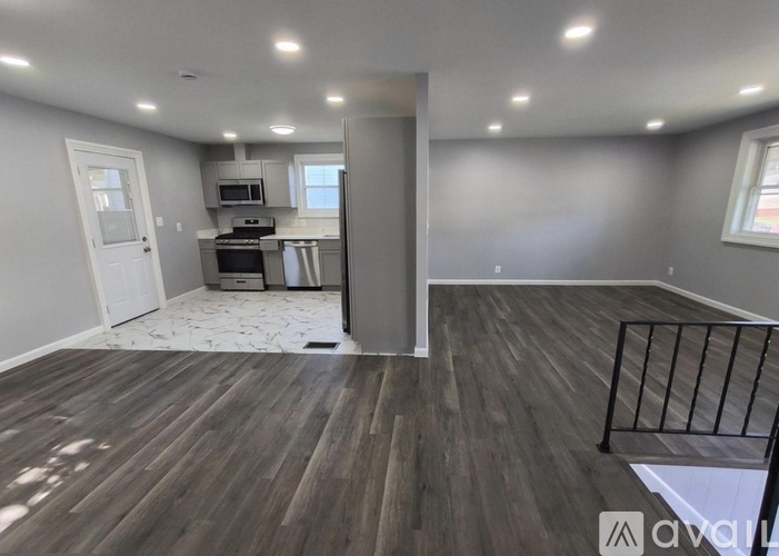 A room with wooden flooring and a kitchen area in the background.