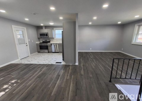 A room with wooden flooring and a kitchen area in the background.