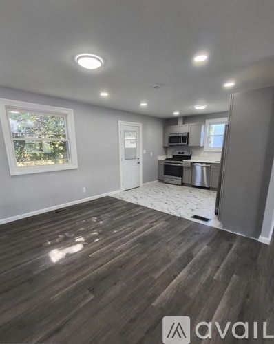 A room with wooden flooring and a kitchen area in the background.