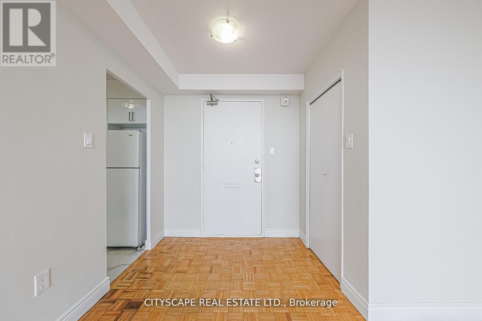 A white hallway with a wooden floor and a door on the right.