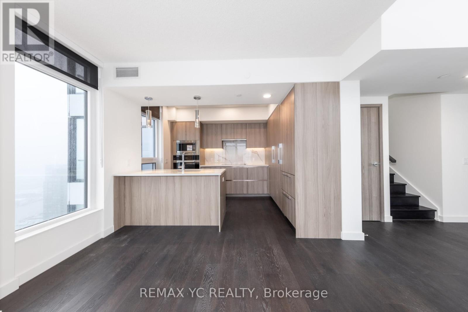 A spacious, well-lit room with a kitchen area and a staircase.