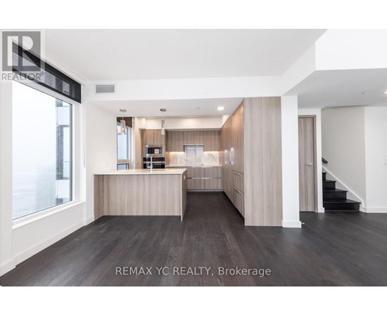 A spacious, well-lit room with a kitchen area and a staircase.
