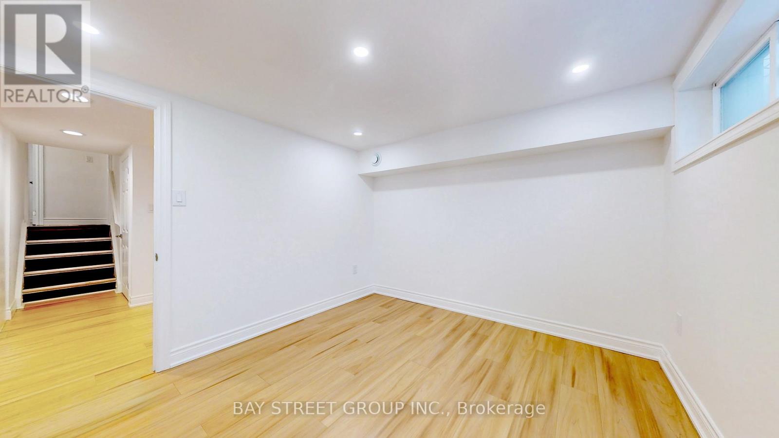 A spacious room with wooden flooring and white walls, with a staircase on the left side.