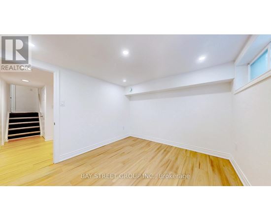 A spacious room with wooden flooring and white walls, with a staircase on the left side.