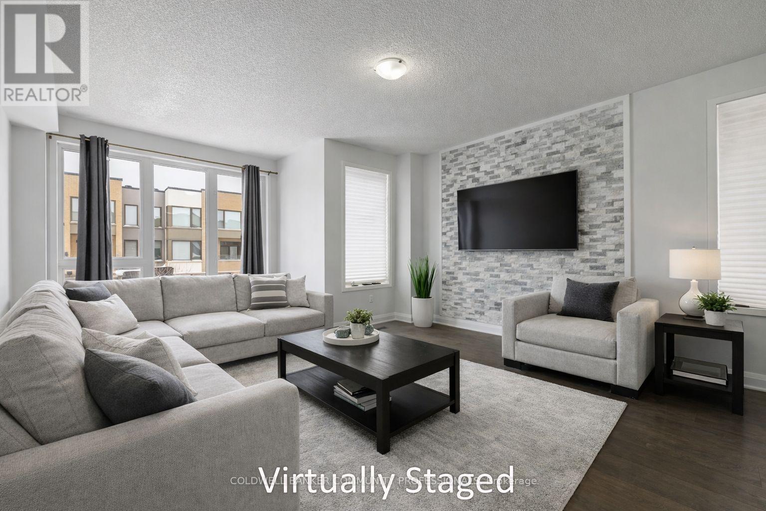 A living room with a grey couch, a black coffee table, a white chair, and a stone wall with a flat screen TV mounted on it.
