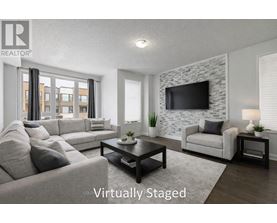 A living room with a grey couch, a black coffee table, a white chair, and a stone wall with a flat screen TV mounted on it.