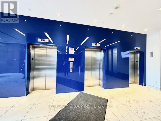 A hallway with blue walls and white floors has three elevators.