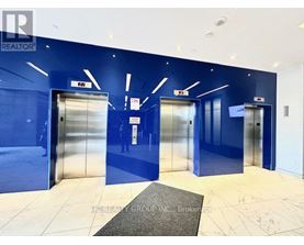A hallway with blue walls and white floors has three elevators.