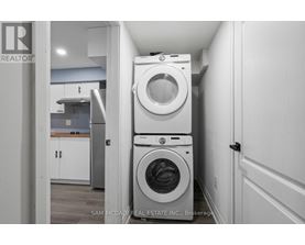 A white washing machine is stacked on top of another white washing machine in a small laundry room.
