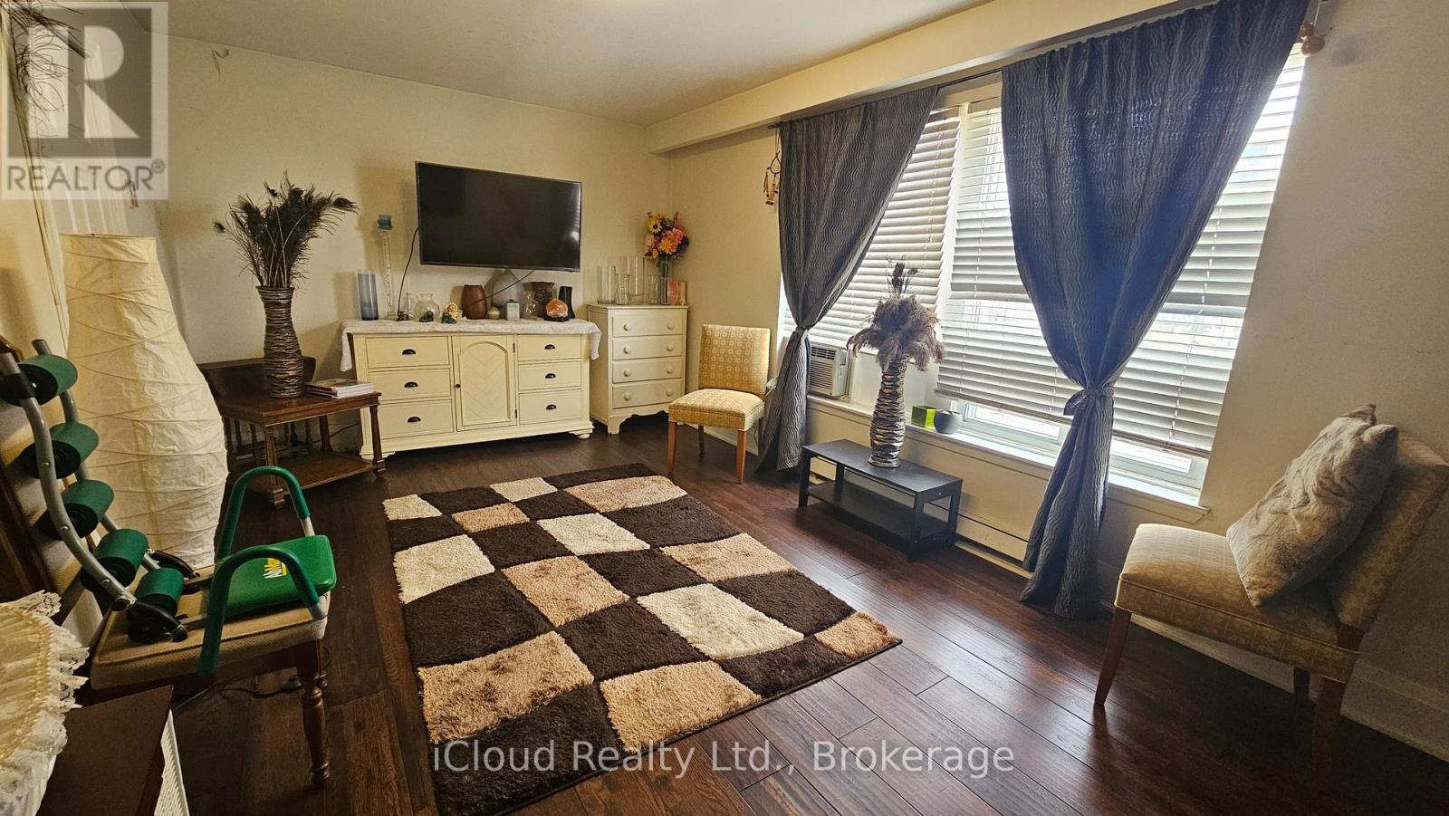A living room with a checkered rug, a green armchair, and a television.
