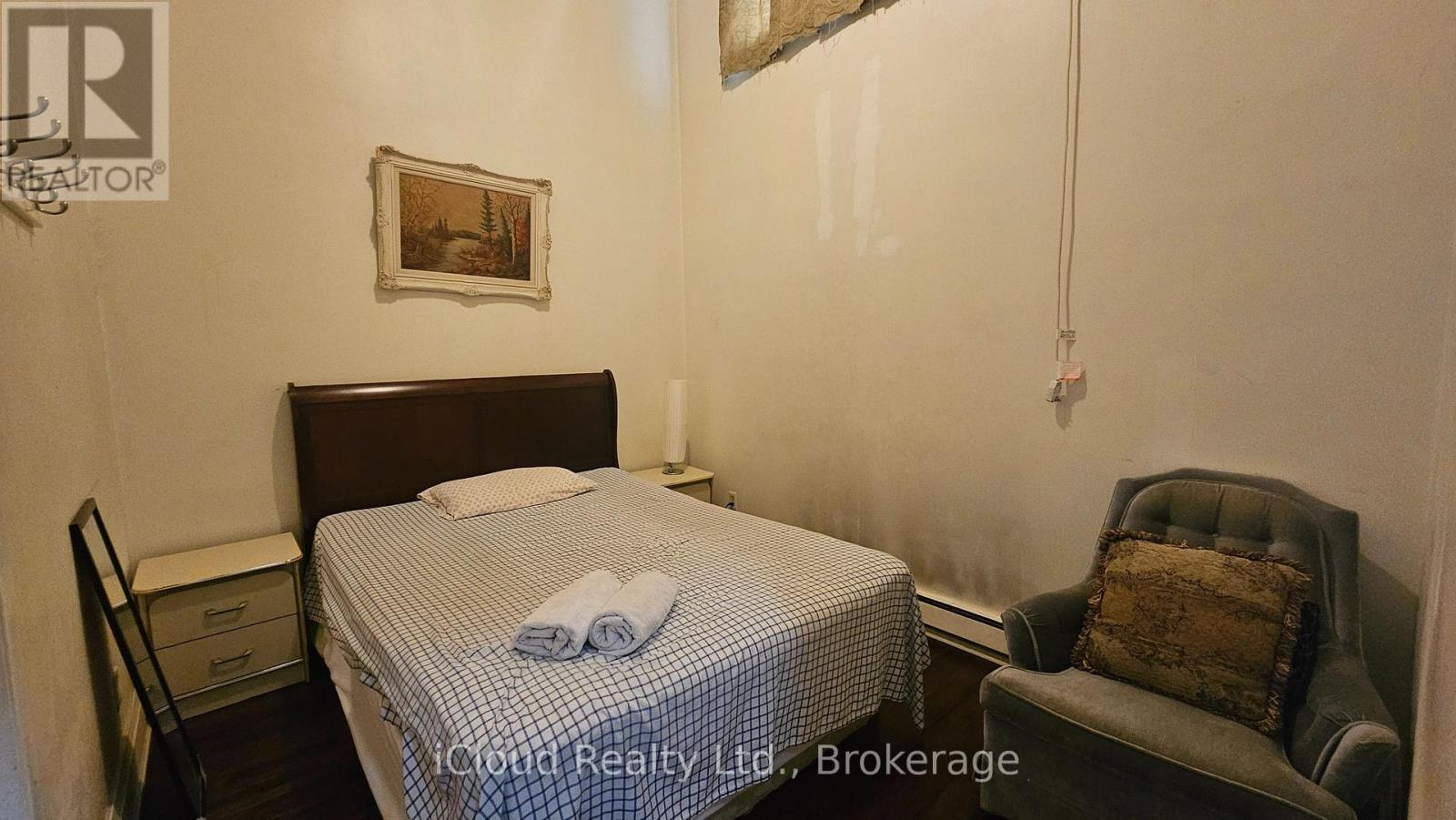 A bedroom with a bed, chair, and picture on the wall.