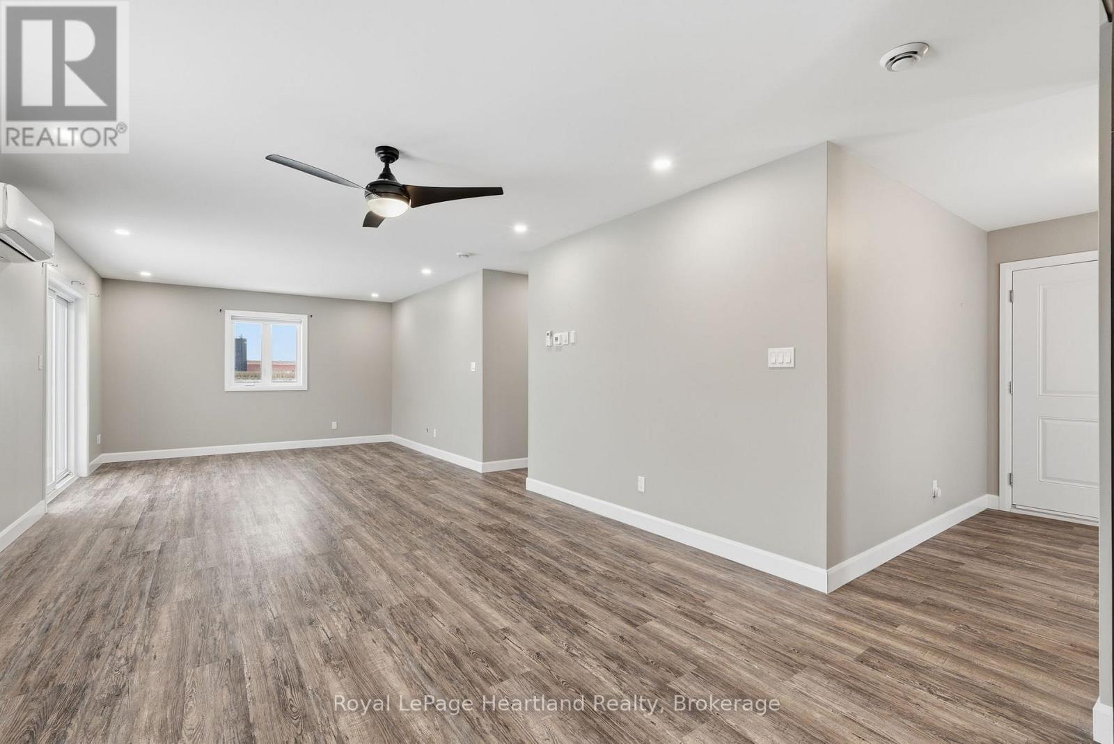 A spacious room with wooden flooring and a ceiling fan.
