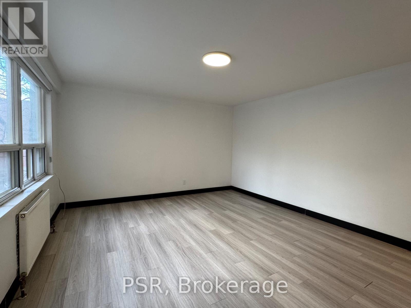 A room with wooden flooring and white walls, with a window on the left side.