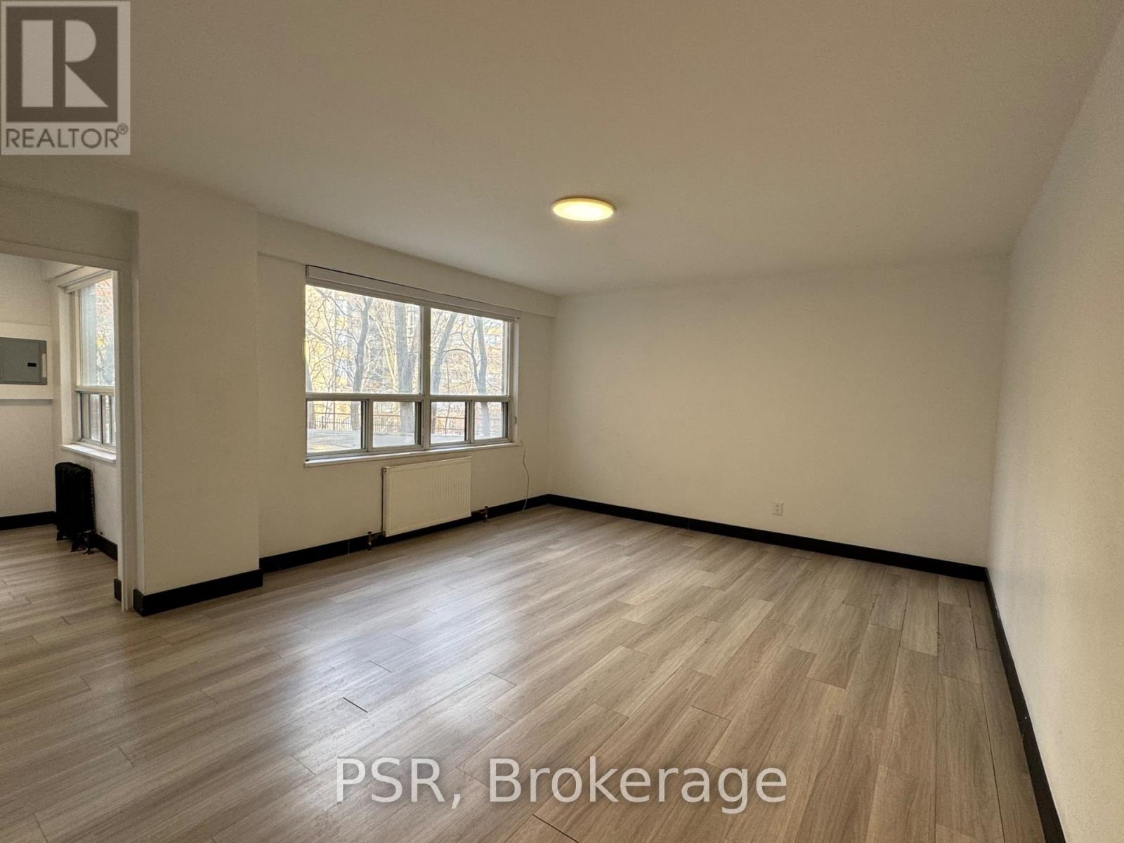 A room with wooden flooring and a window with a view of trees outside.