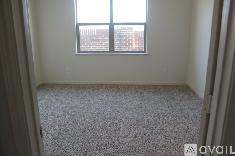 A carpeted room with a window and a view of a brick building outside.